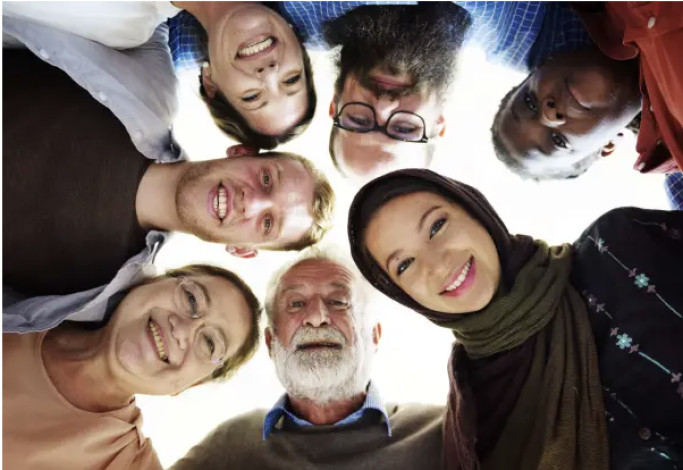 A diverse group of people look down toward the camera, arranged in a circle.